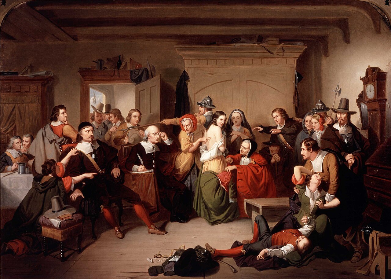 A painting of a woman being examined for witch's marks before a crowd of Puritan men