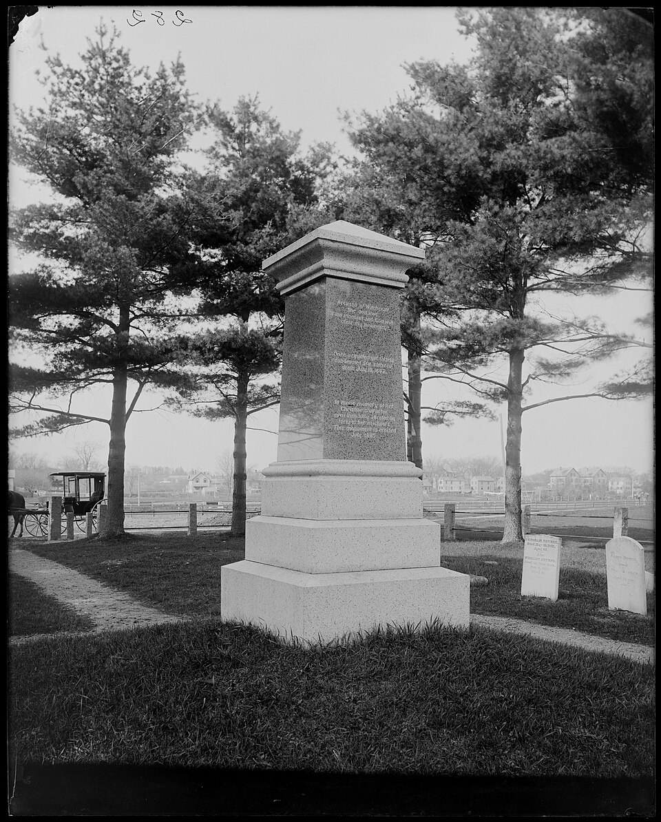 A granite monument on a stepped base among pine trees